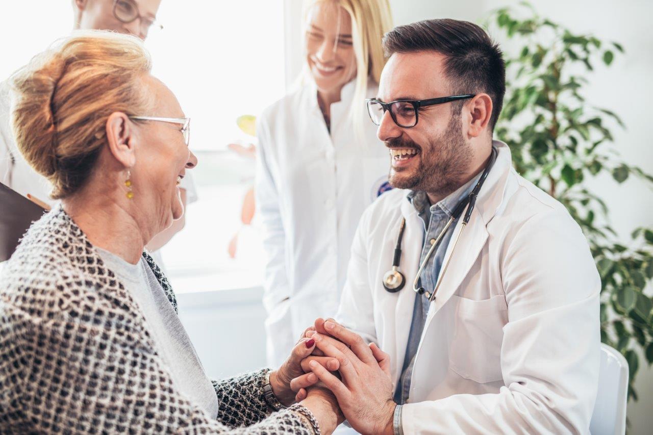 Smiling doctor holding elderly patients hand